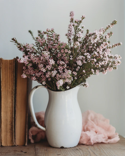 a white pitcher filled with flowers next to a book