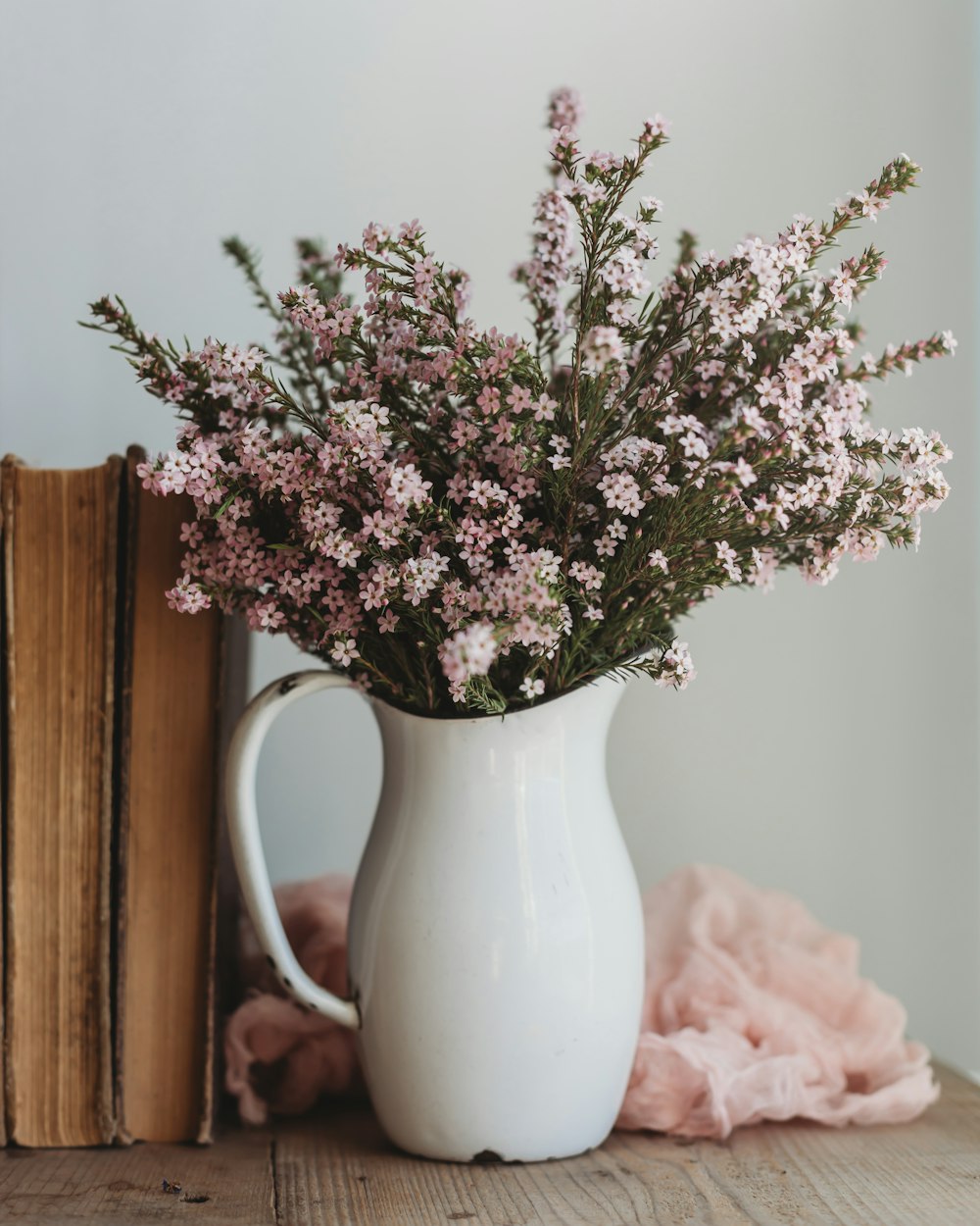 a white pitcher filled with flowers next to a book