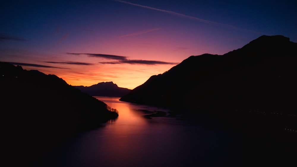 una puesta de sol sobre un cuerpo de agua con montañas de fondo