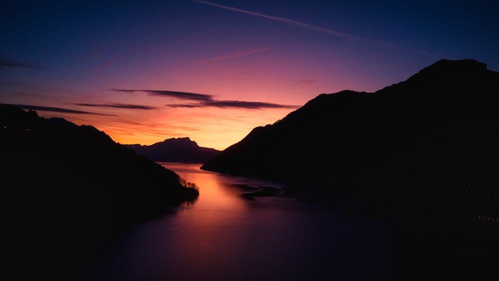 a sunset over a body of water with mountains in the background