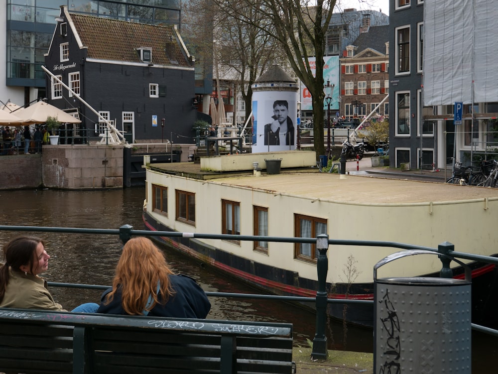 two people sitting on a bench looking at a boat