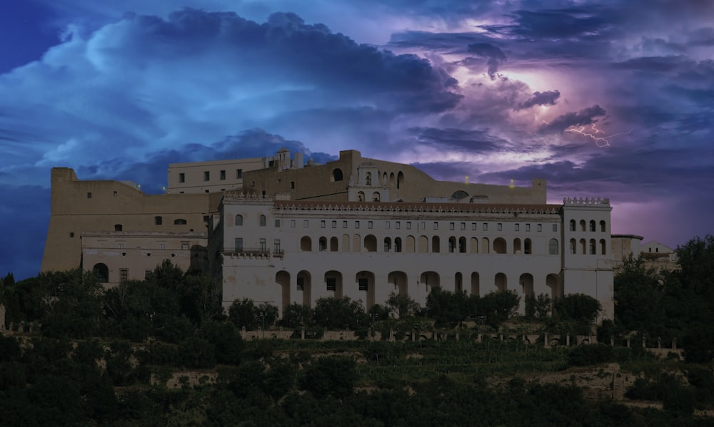 a large white building sitting on top of a hill under a cloudy sky