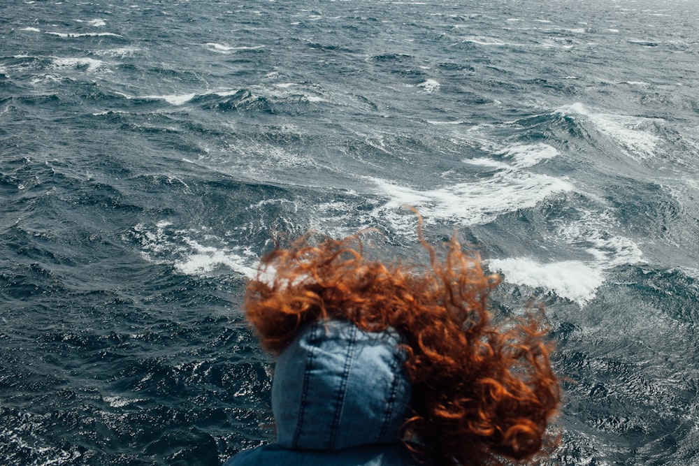 a woman with red hair standing on a boat in the ocean