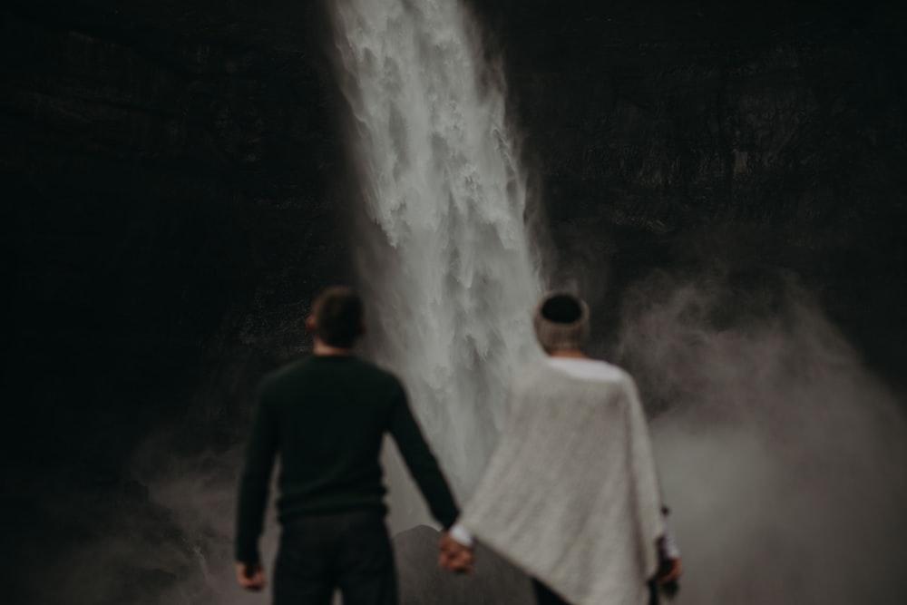 a man and a woman standing in front of a waterfall