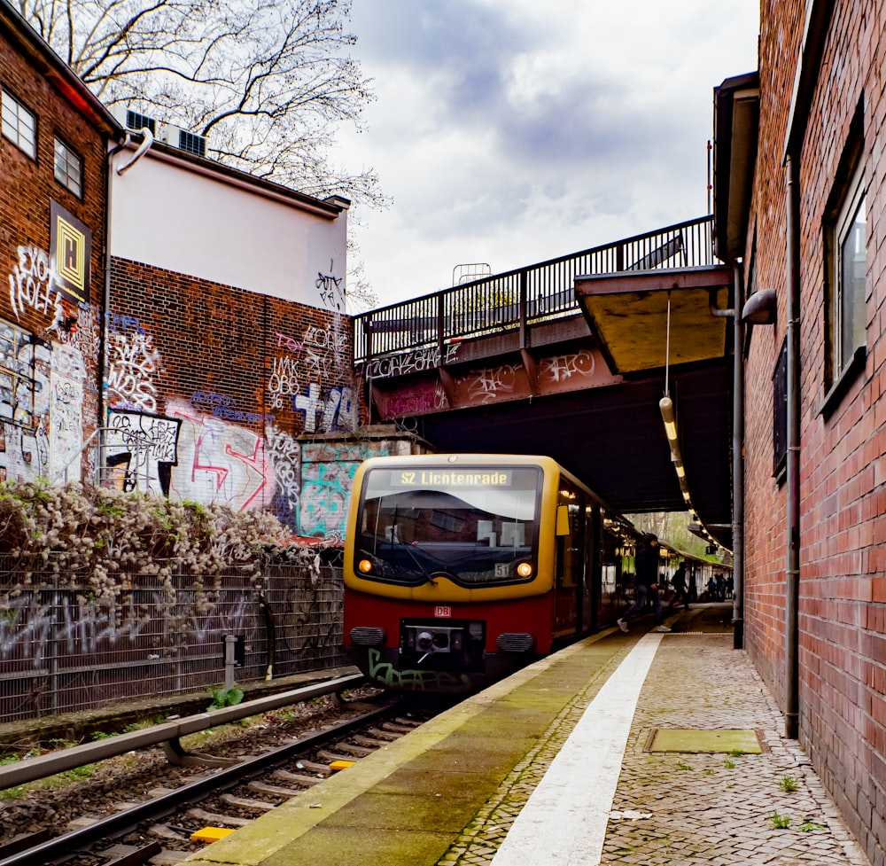 a yellow and red train traveling under a bridge