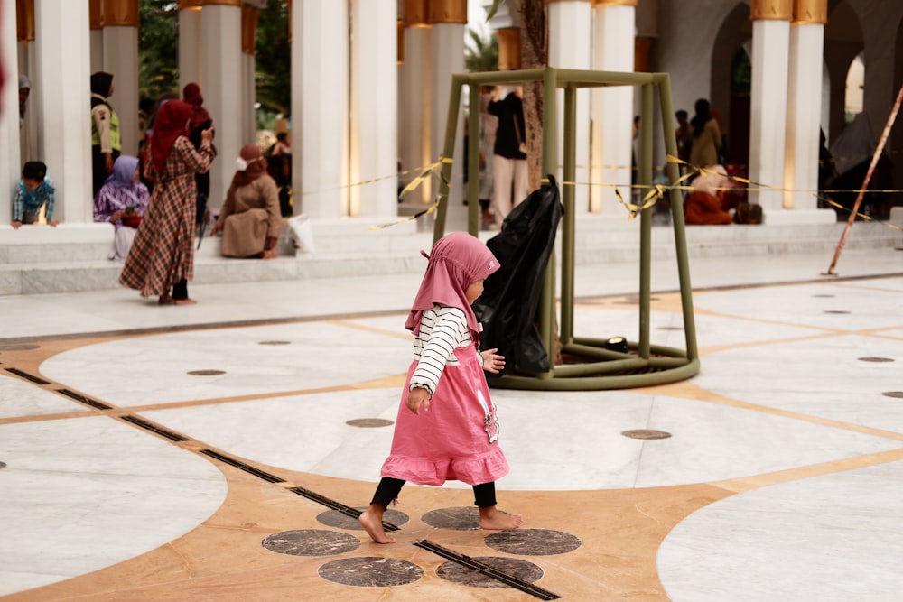 a little girl in a pink hijab walking through a building