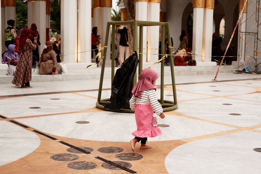 a little girl in a pink hijab walking towards a swing set