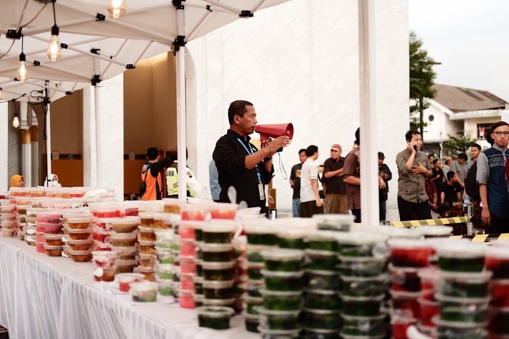 a man speaking into a megaphone in front of a table of food