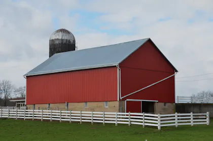 Red barn with a white fence and silo