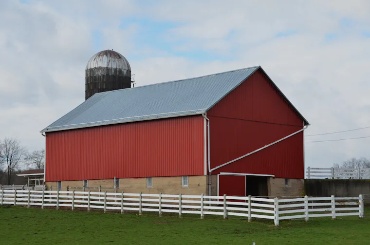 Red barn with a white fence and silo