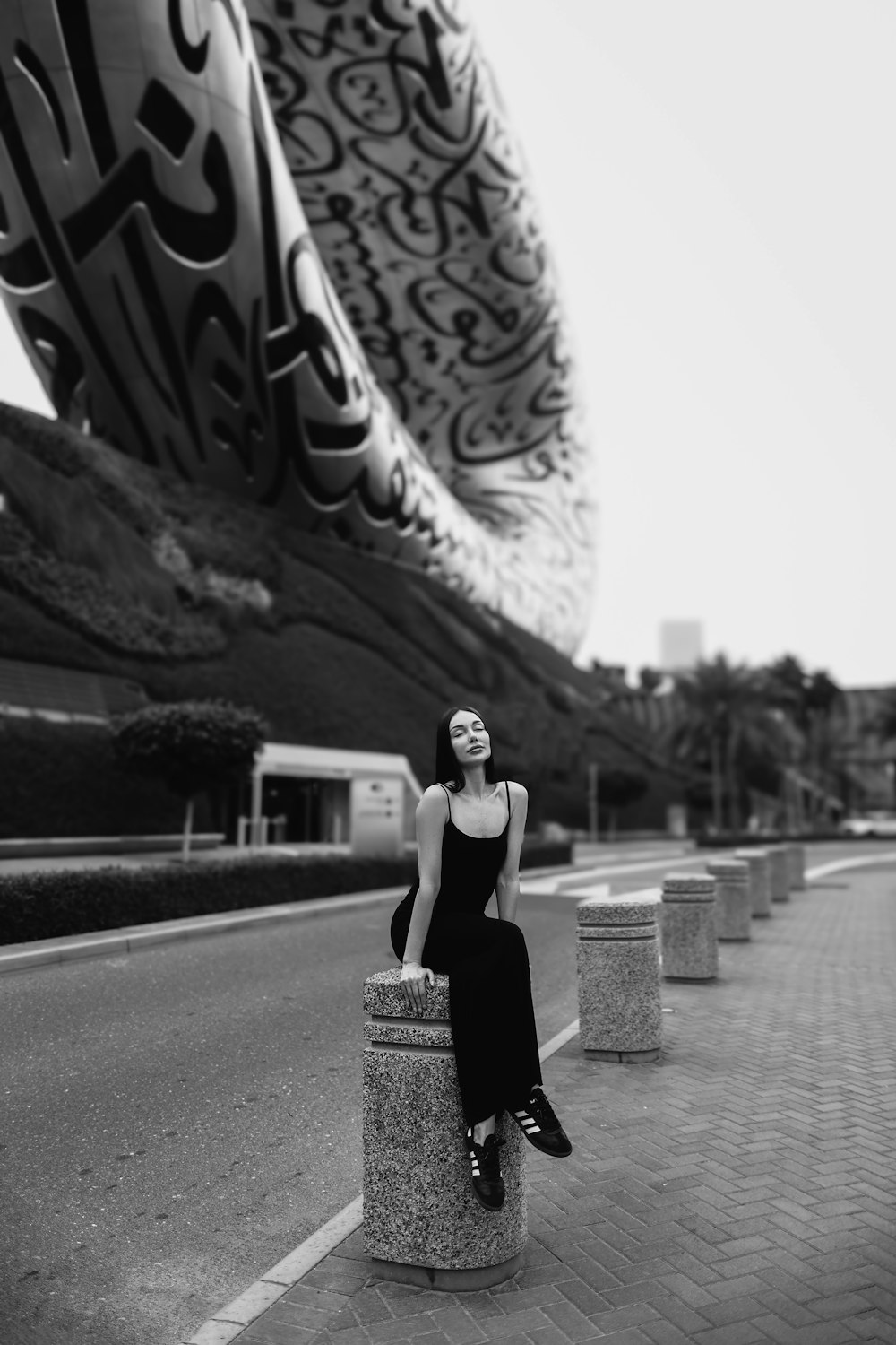 a woman sitting on a pillar in front of a building