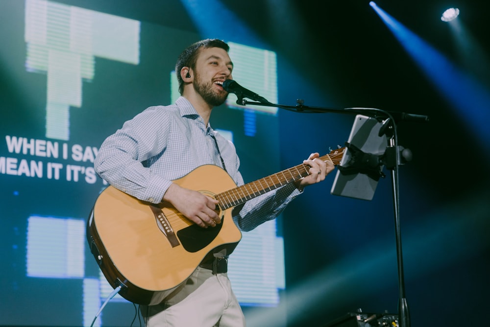 Un hombre sosteniendo una guitarra mientras está de pie frente a un micrófono