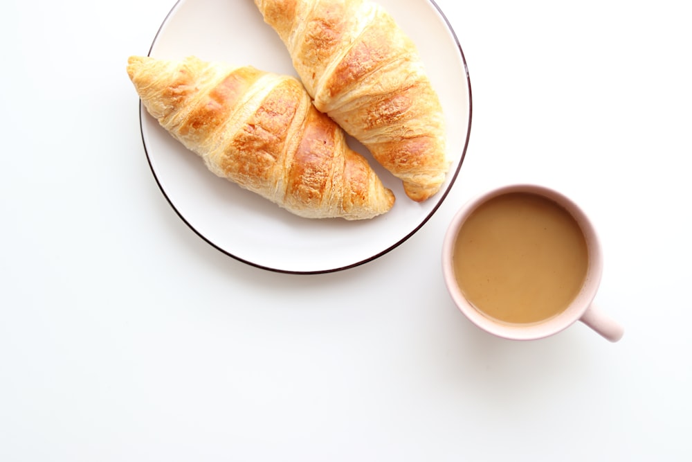 due croissant su un piatto accanto a una tazza di caffè