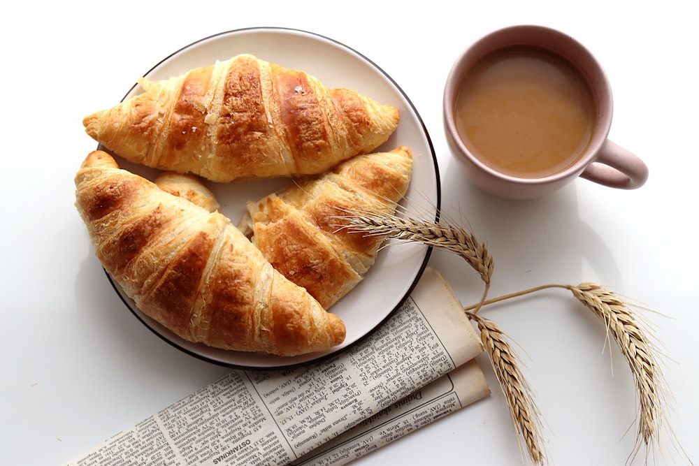 um prato branco coberto com croissants ao lado de uma xícara de café