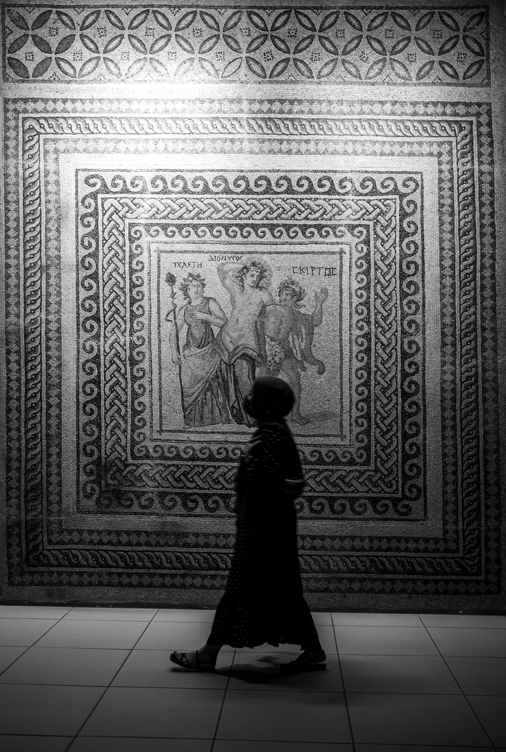 a woman is walking in front of a mosaic