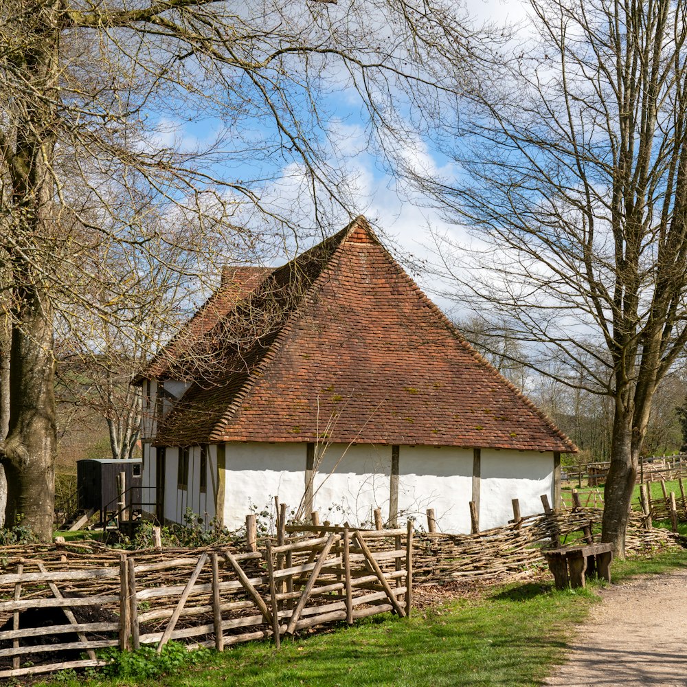 a white building with a brown roof next to a tree