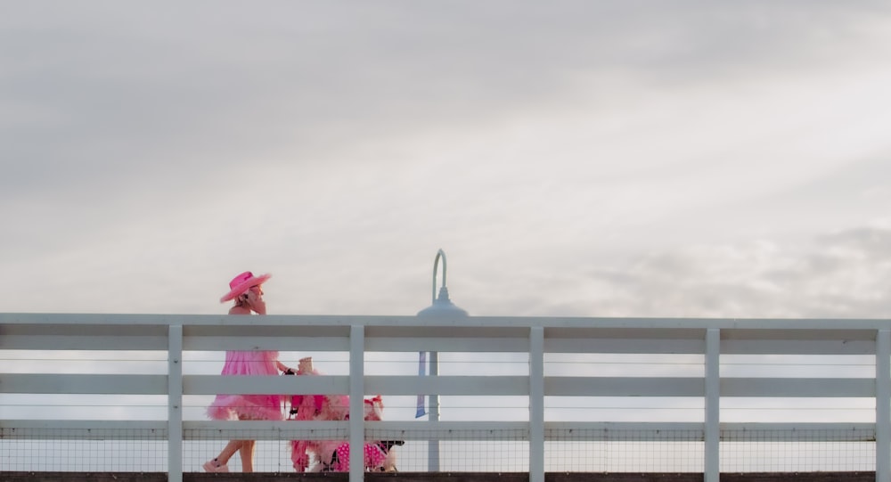 a woman in a pink dress walking across a bridge
