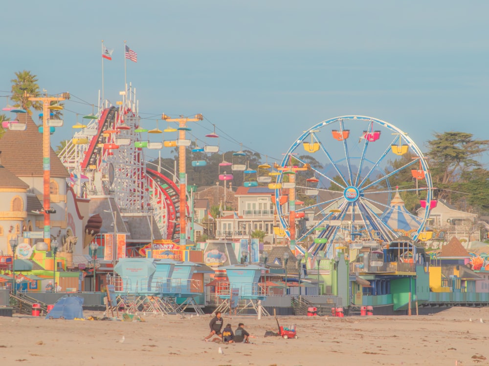 a group of people sitting on a beach next to a ferris wheel