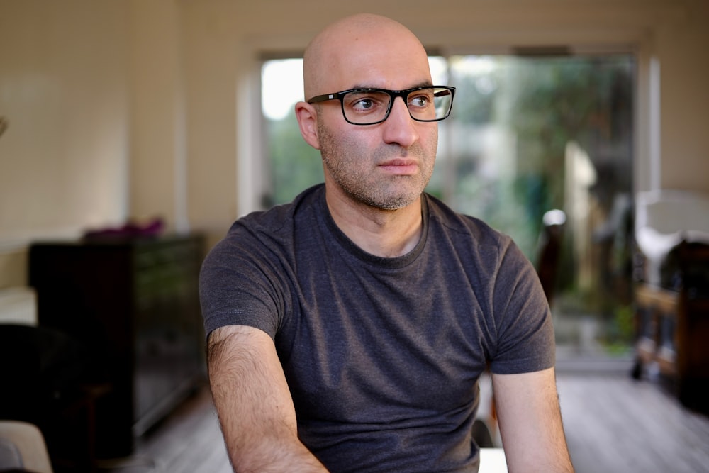 a bald man wearing glasses sitting in a living room