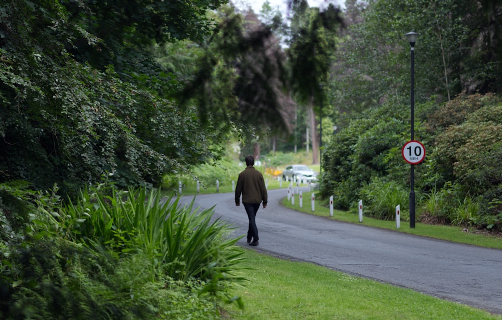 a man walking down a street next to a lush green forest