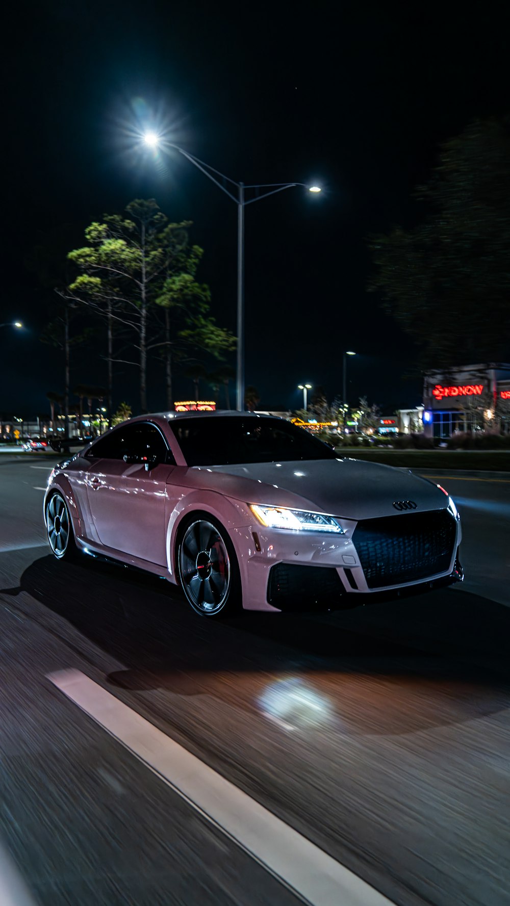 a pink car driving down a street at night