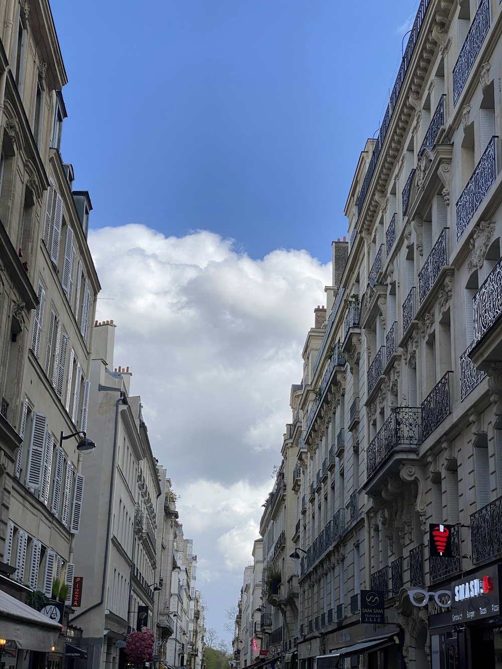 a city street lined with tall buildings under a cloudy blue sky