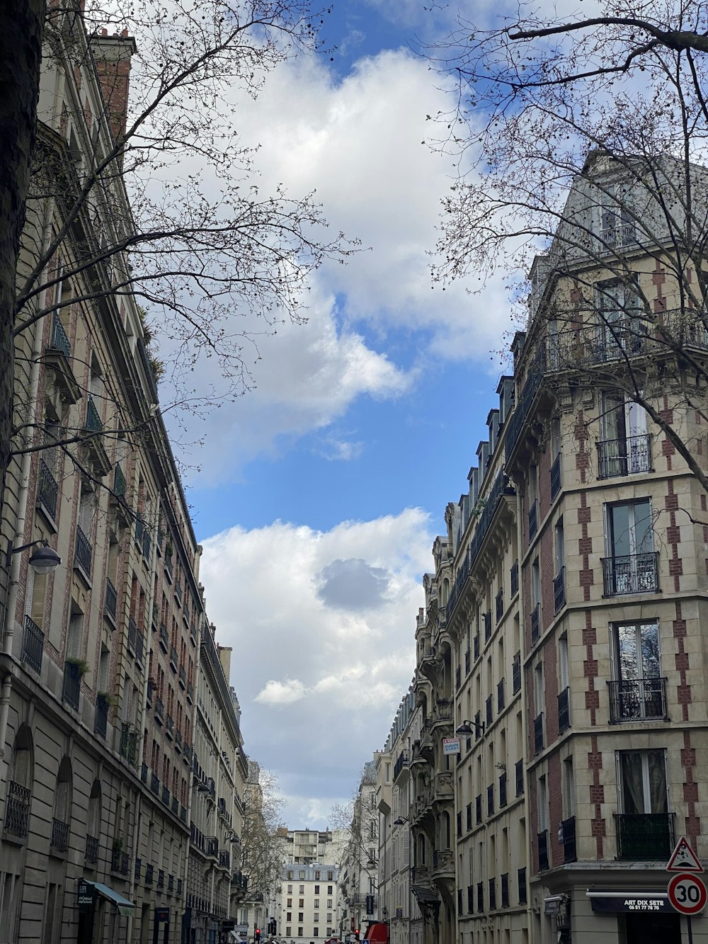 a city street lined with tall buildings under a cloudy blue sky