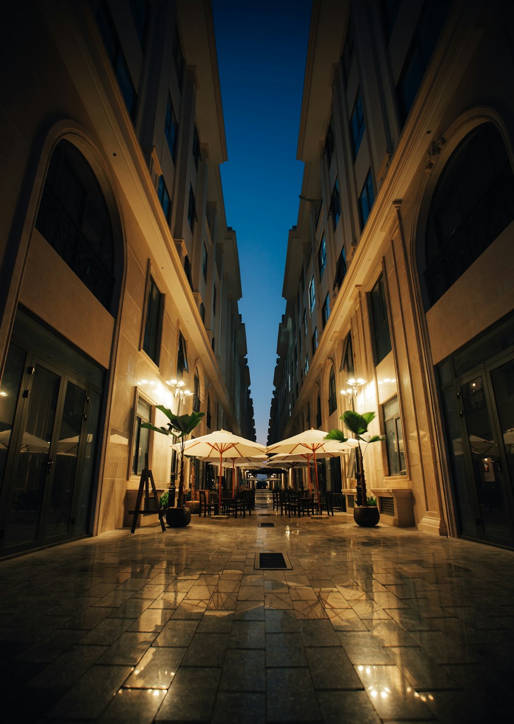 an empty courtyard with tables and umbrellas lit up at night
