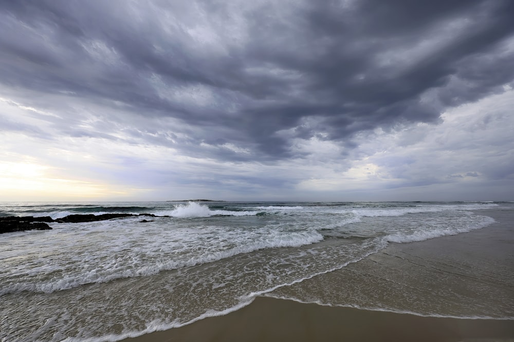 a cloudy day at the beach with waves coming in