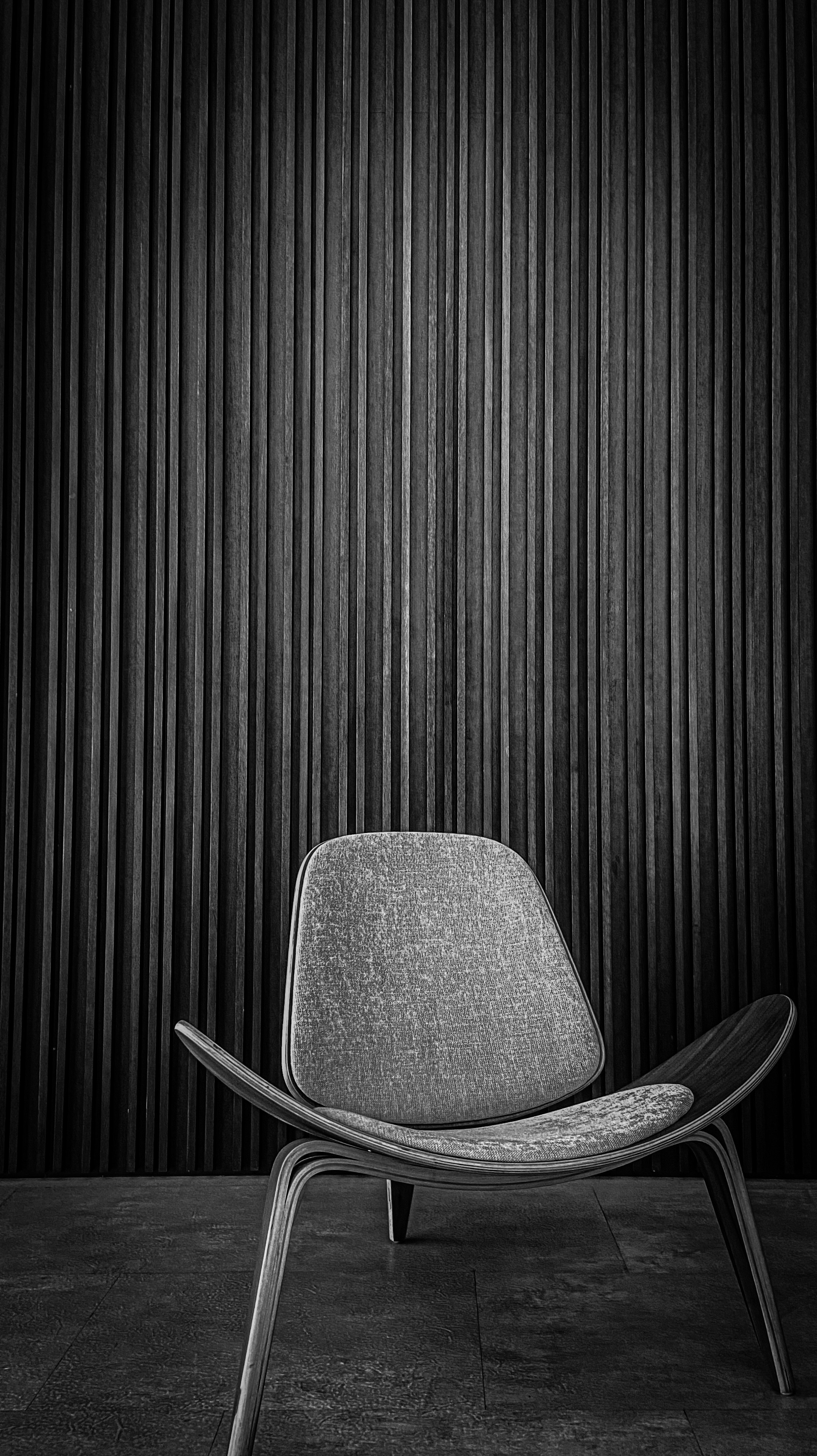 Minimal leather armchair in a moody dark room with dramatic side lighting and deep espresso wood paneling