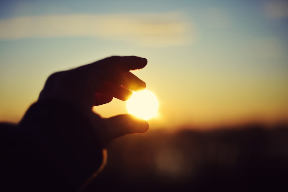 a person holding their hand up to the sun