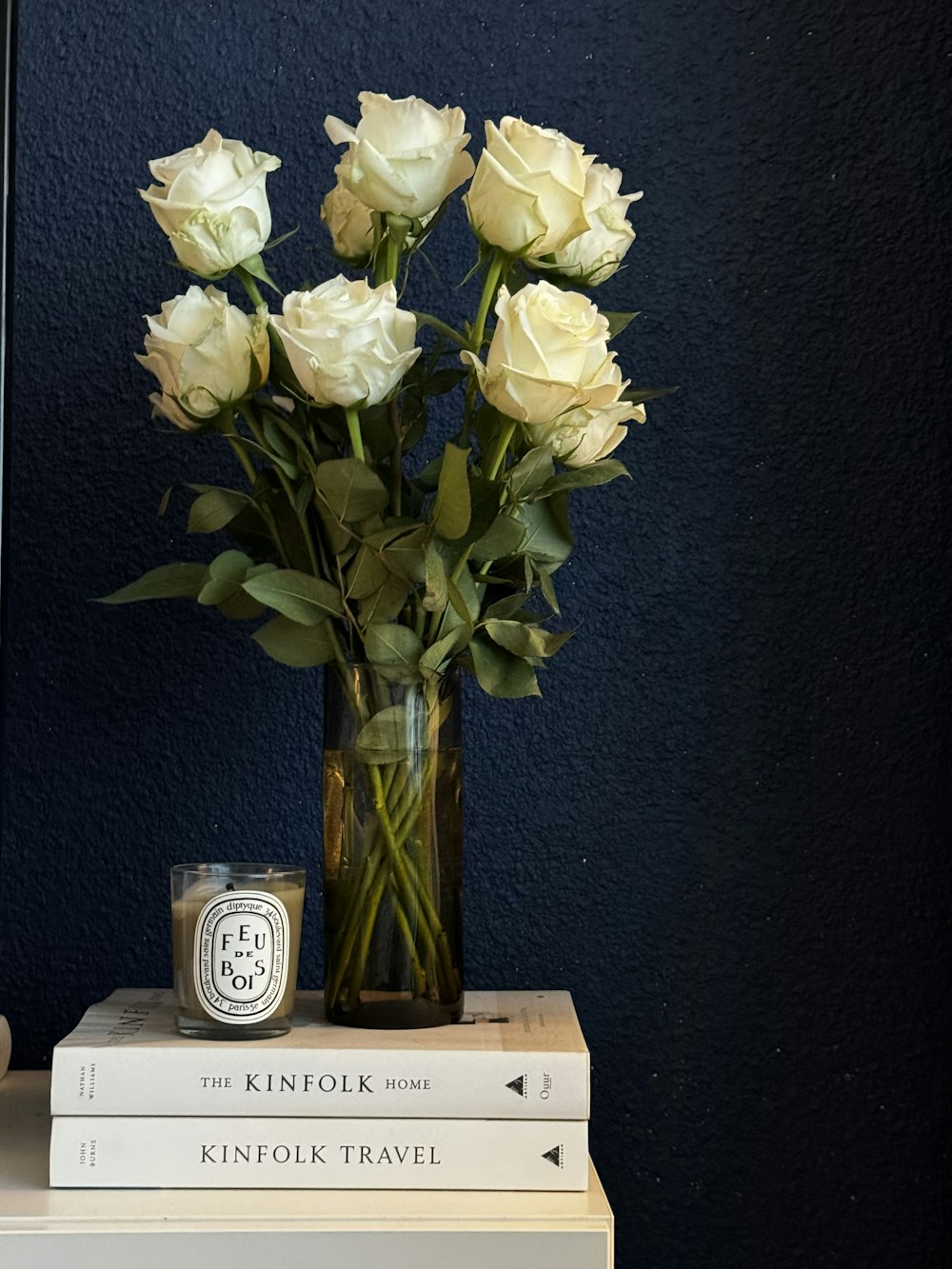 a vase filled with white roses sitting on top of a stack of books