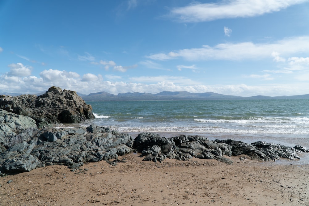 a rocky beach with a body of water and mountains in the distance