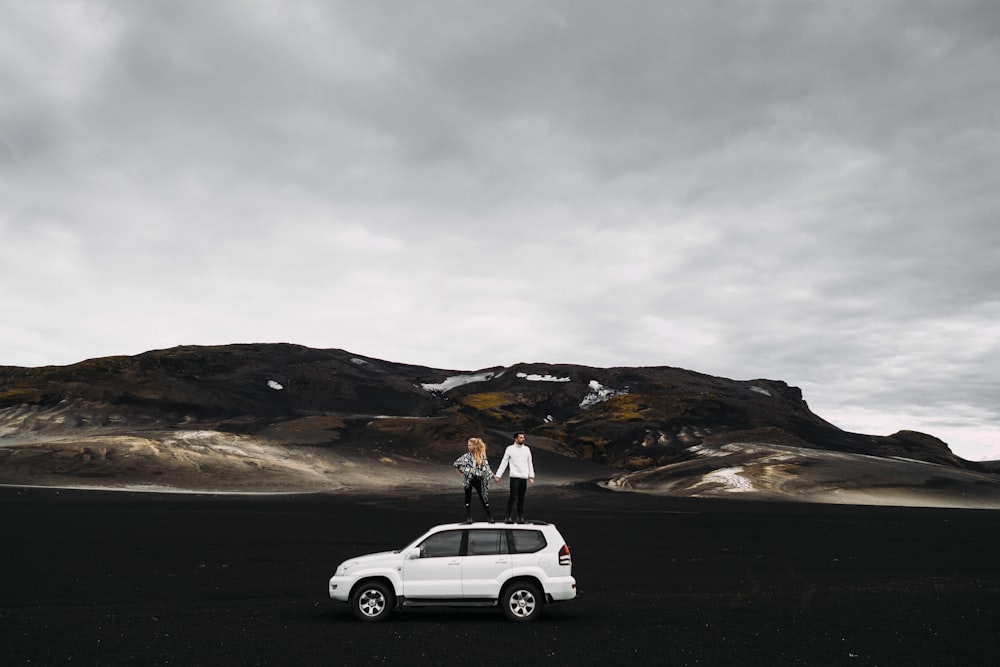 two people standing on top of a white car