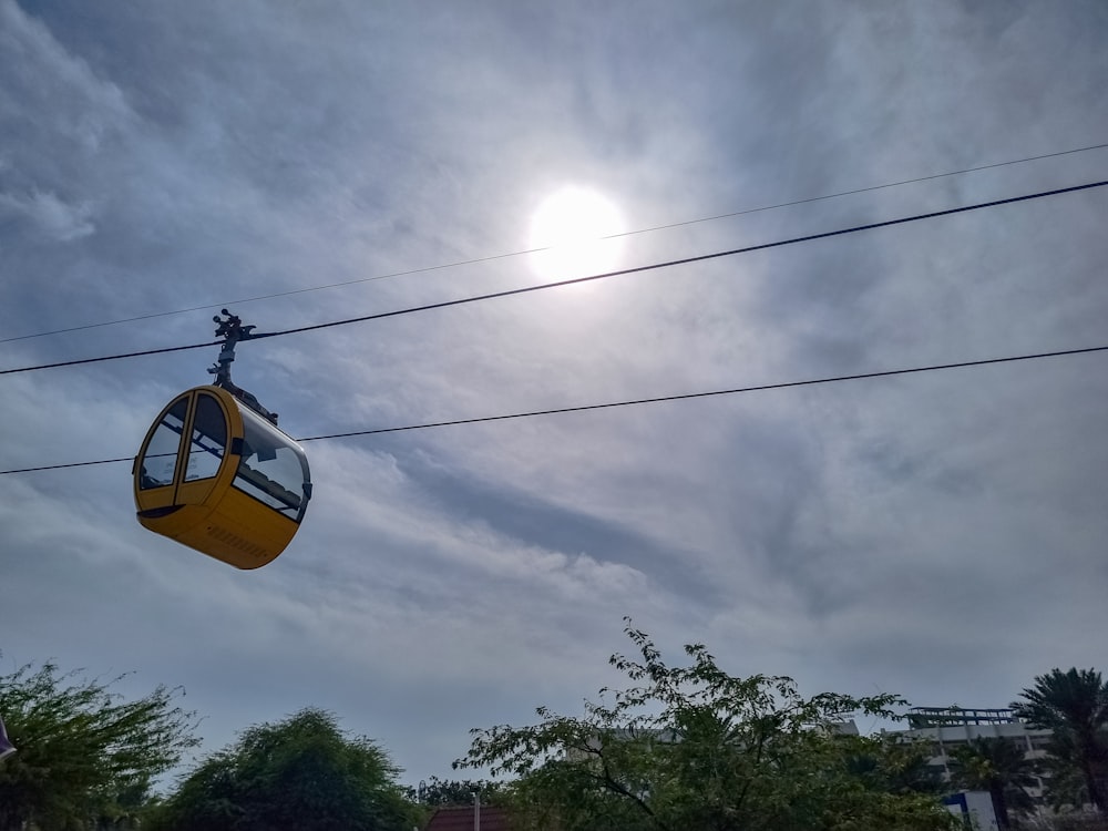 a yellow cable car going through a cloudy sky