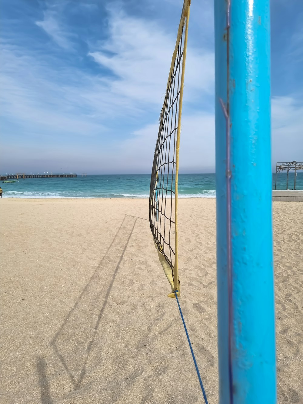 a blue pole on a beach with a volleyball net