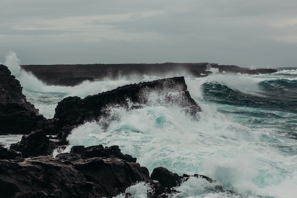 a large wave crashes against a rocky shore