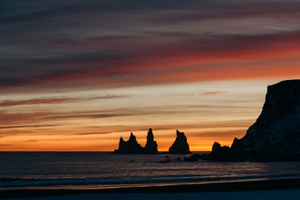 the sun is setting over the ocean with rocks in the foreground