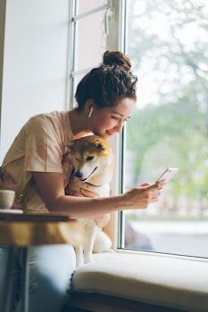 a woman sitting on a window sill holding a dog