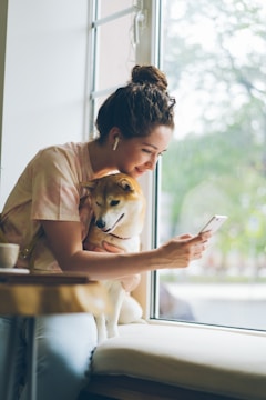 a woman sitting on a window sill holding a dog