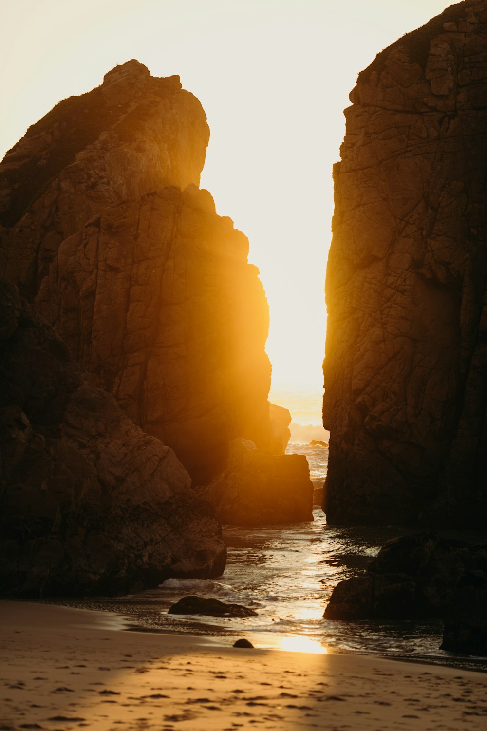 el sol se está poniendo en la playa junto a las rocas