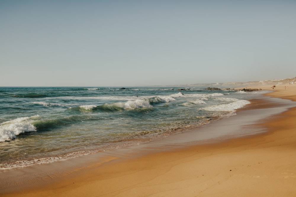 uma praia de areia com ondas entrando e saindo da água