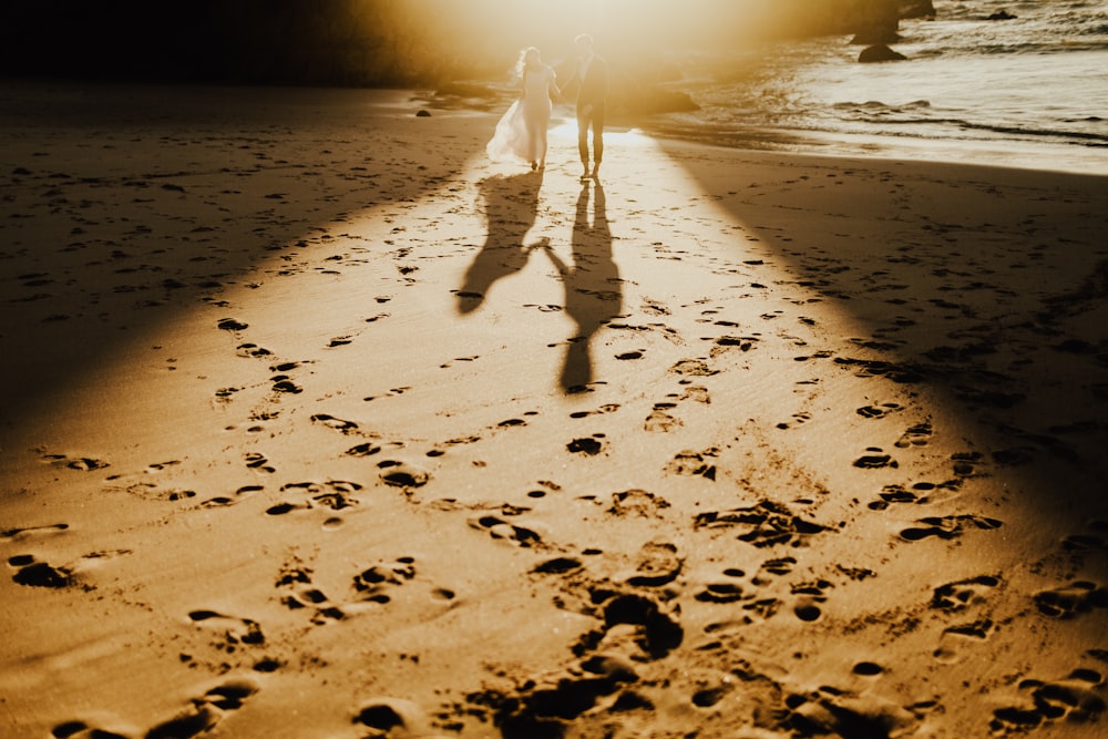 a couple of people walking down a beach next to the ocean