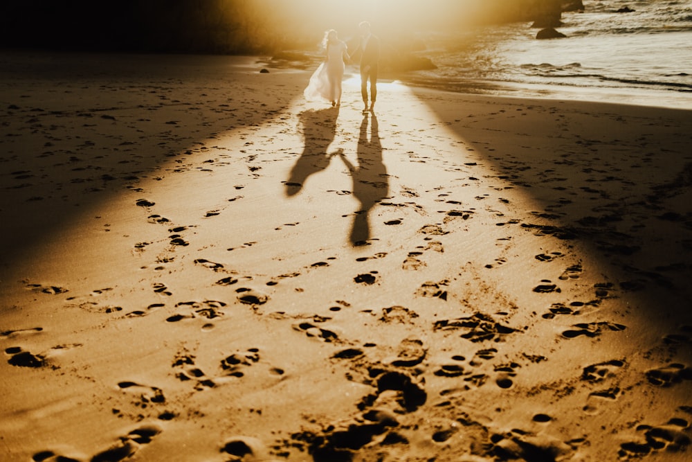 un couple de personnes marchant sur une plage à côté de l’océan
