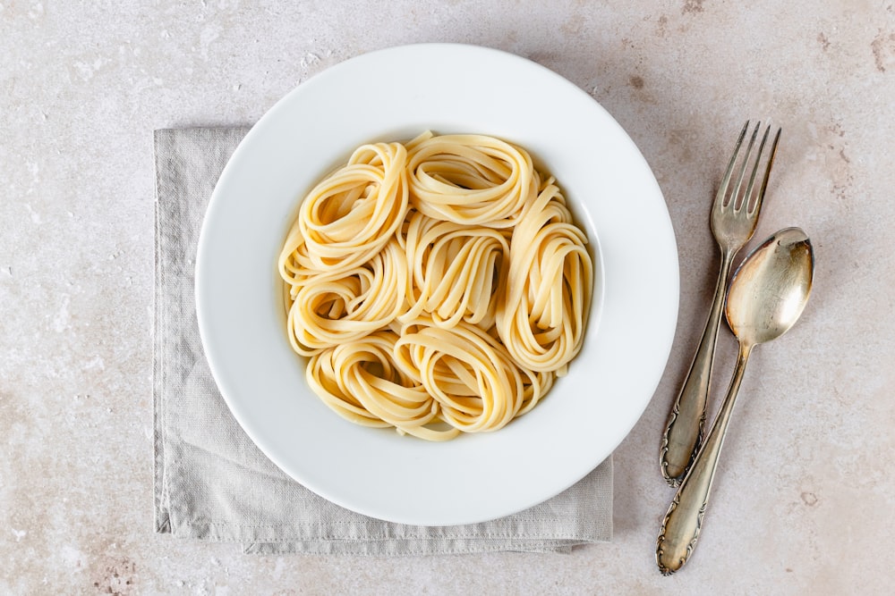 a plate of pasta on a napkin next to a fork and knife