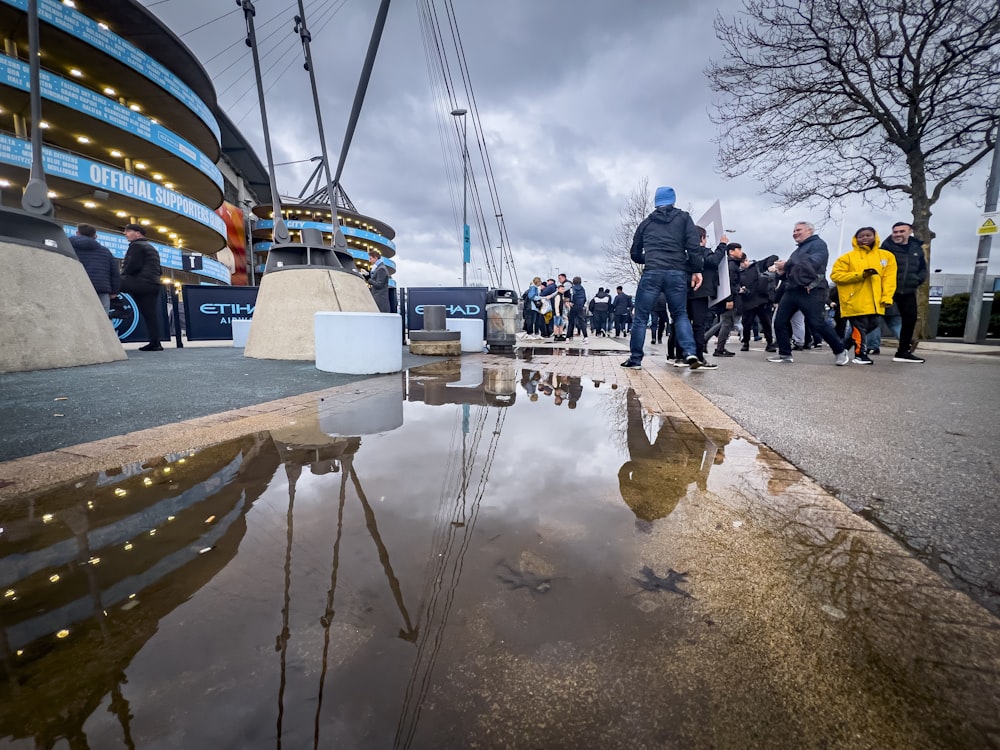 a group of people walking down a street next to a puddle