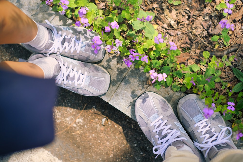 a pair of feet standing on a sidewalk next to purple flowers
