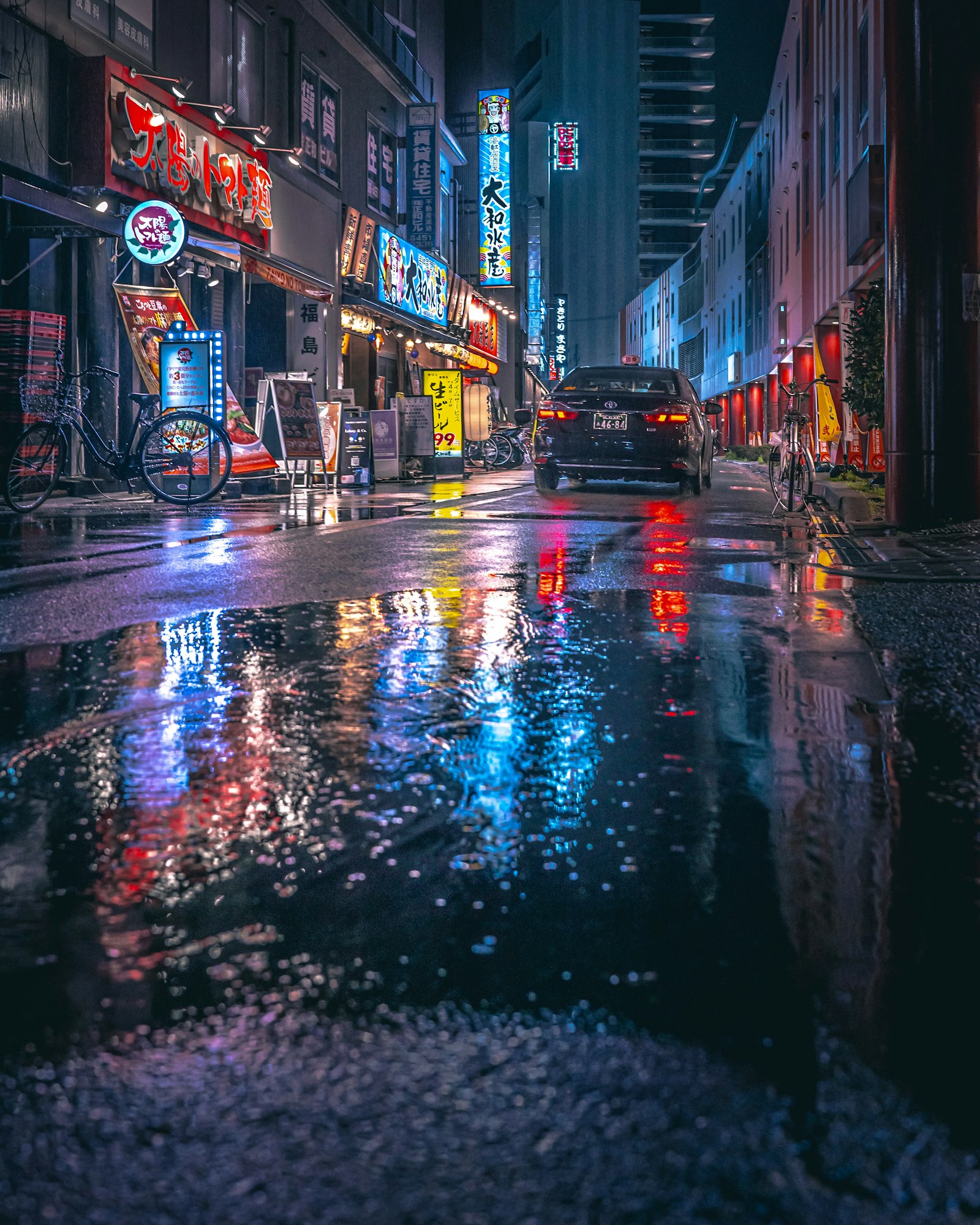 A city street at night with rain puddles reflecting the lights, Osaka