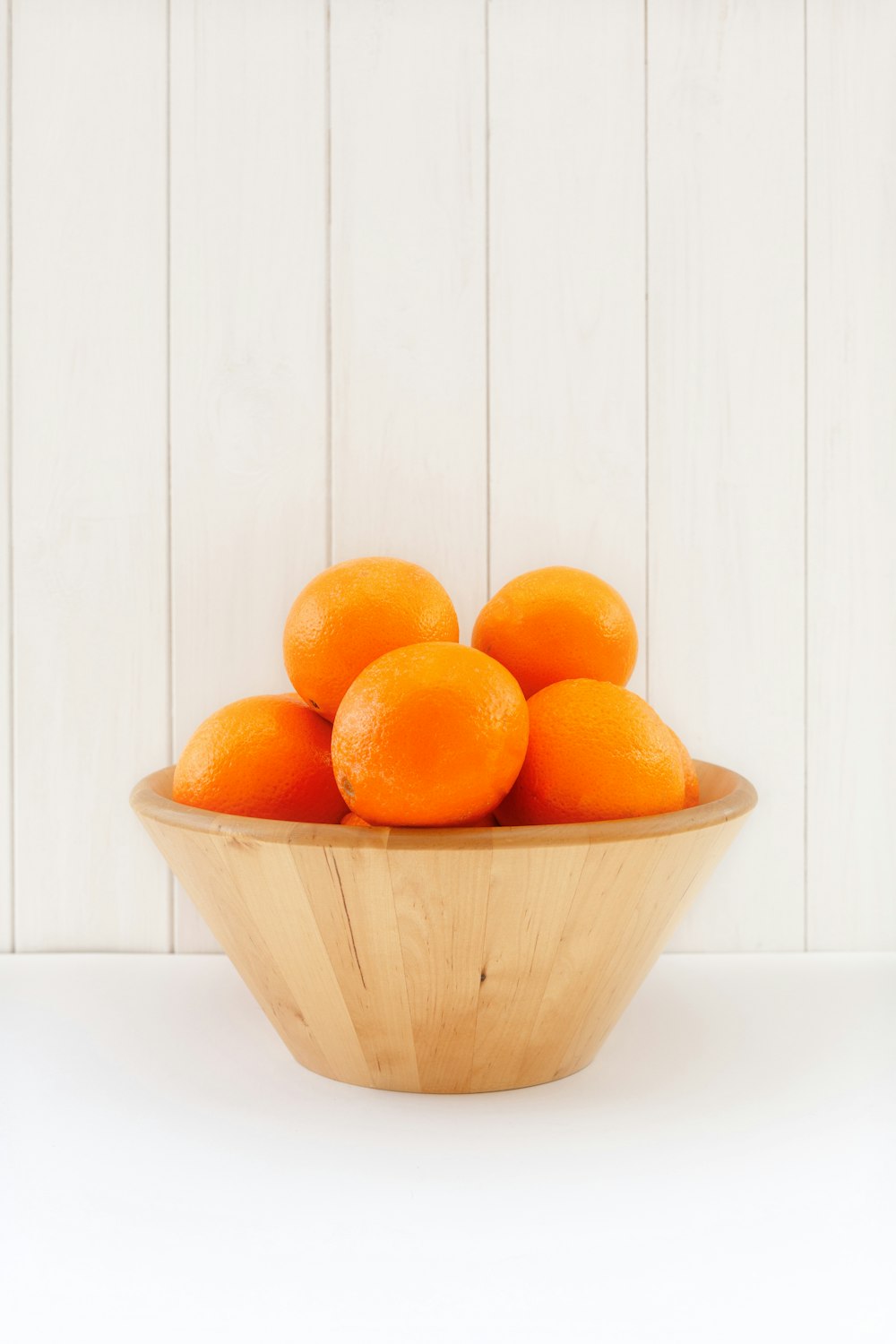 a wooden bowl filled with oranges on top of a table