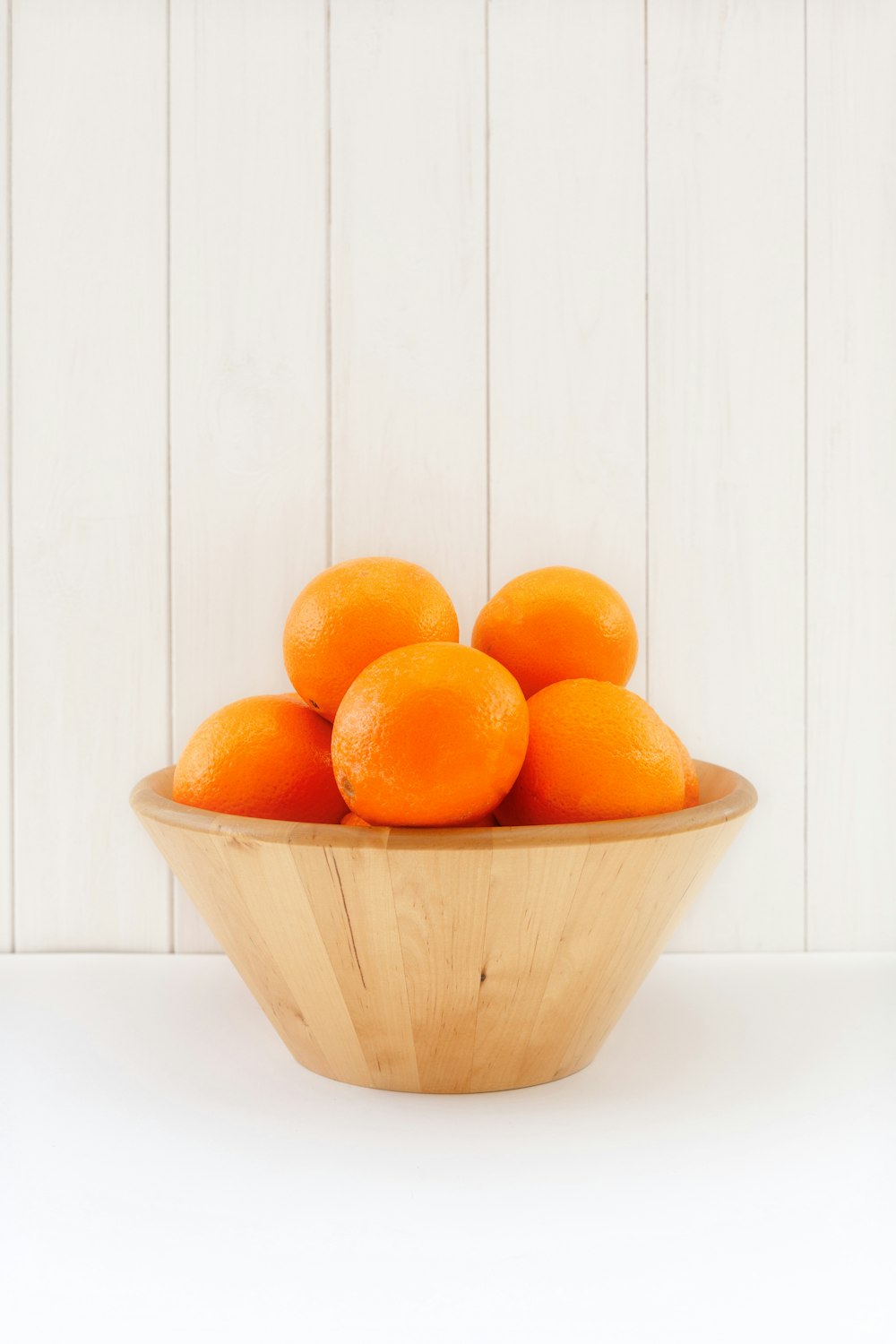 un bol en bois rempli d’oranges sur le dessus d’une table